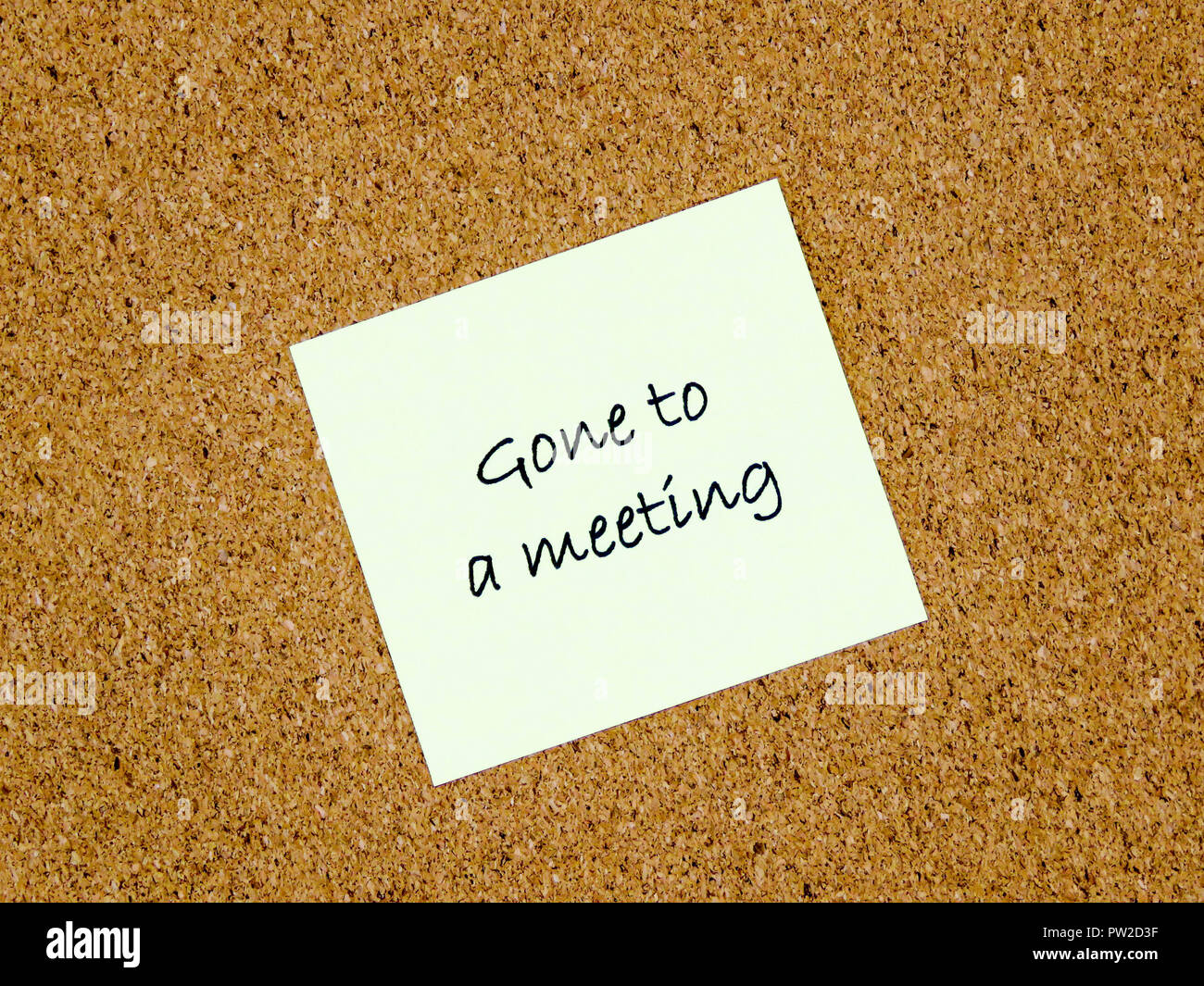 A yellow sticky note with gone to a meeting written on it on a cork