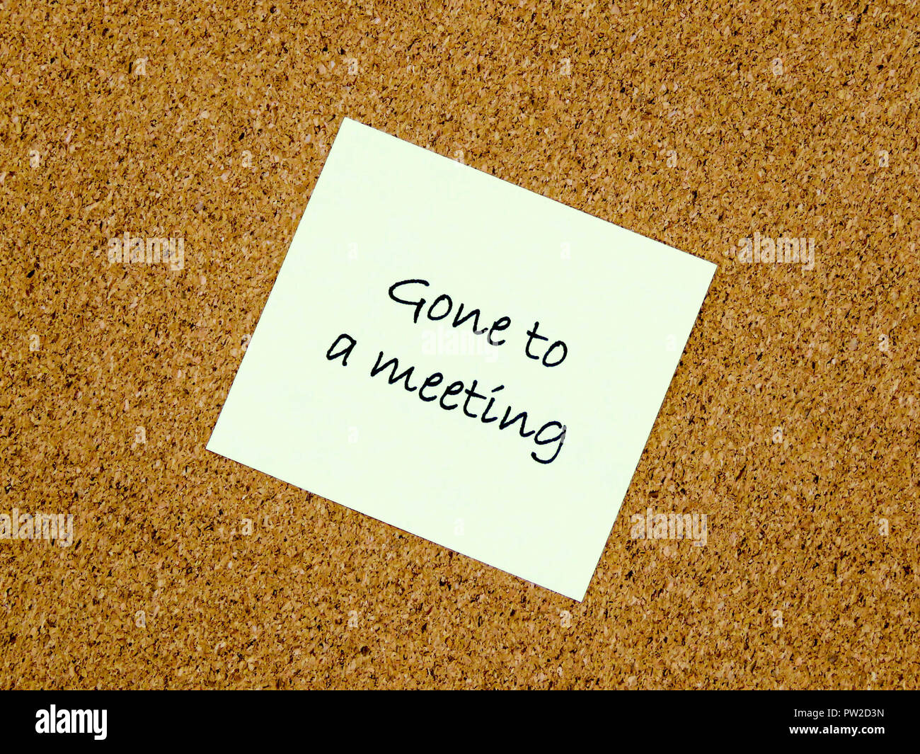 A yellow sticky note with gone to a meeting written on it on a cork