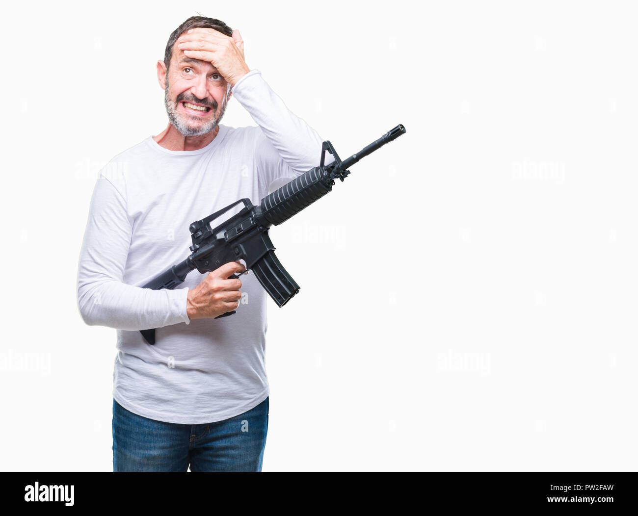 Middle age senior hoary criminal man holding gun weapon over isolated background stressed with hand on head, shocked with shame and surprise face, ang Stock Photo