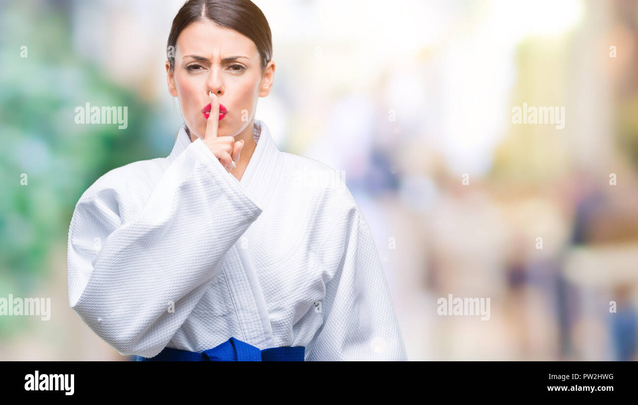 Young beautiful woman wearing karate kimono uniform over isolated background asking to be quiet with finger on lips. Silence and secret concept. Stock Photo