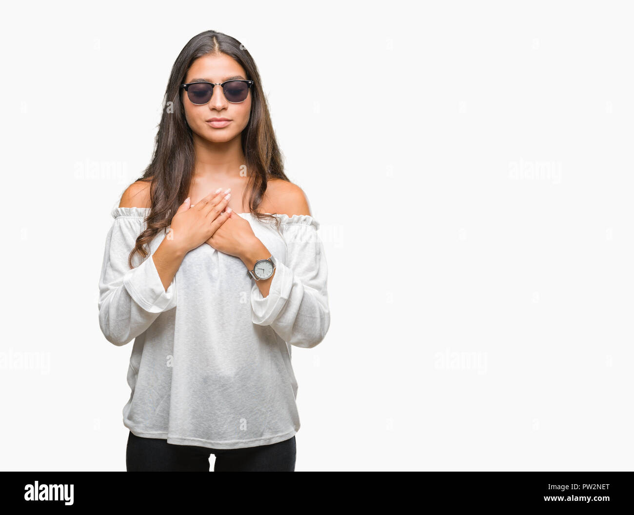 Young beautiful arab woman wearing sunglasses over isolated background smiling with hands on chest with closed eyes and grateful gesture on face. Heal Stock Photo