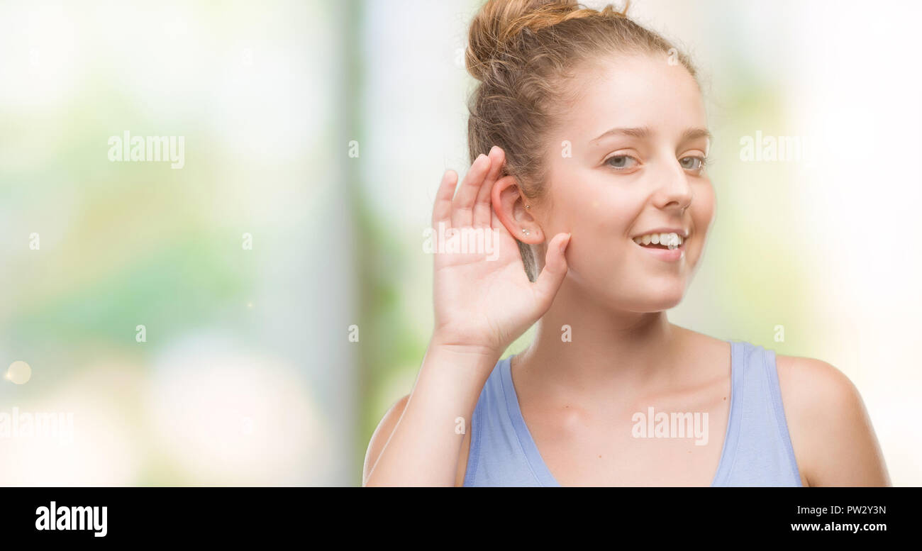 Young blonde woman smiling with hand over ear listening an hearing to rumor or gossip. Deafness concept. Stock Photo