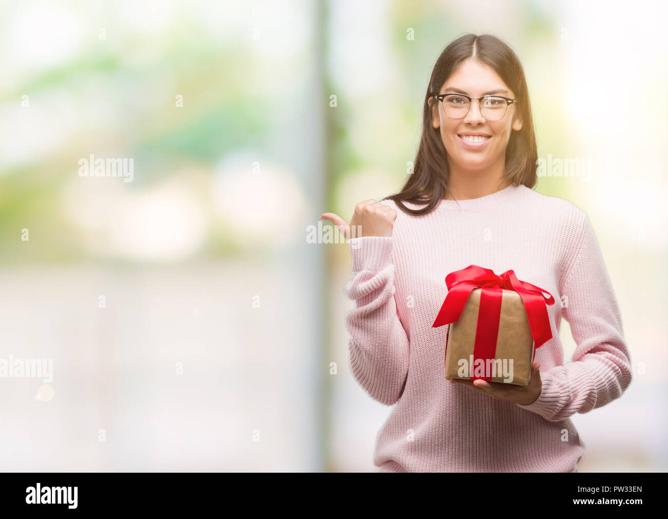 Young hispanic woman holding a gift pointing and showing with thumb up ...