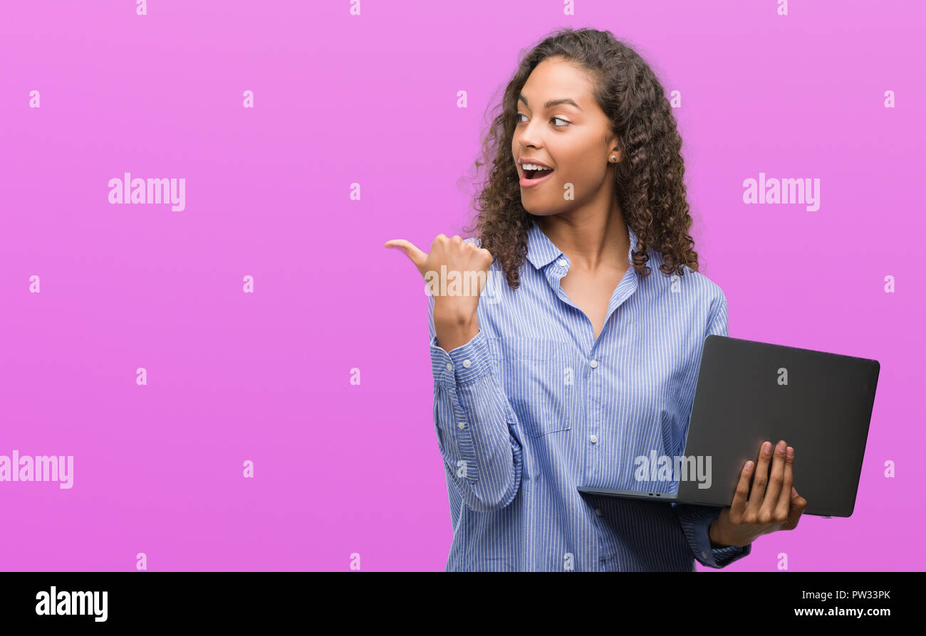Young hispanic woman holding computer laptop pointing and showing with ...