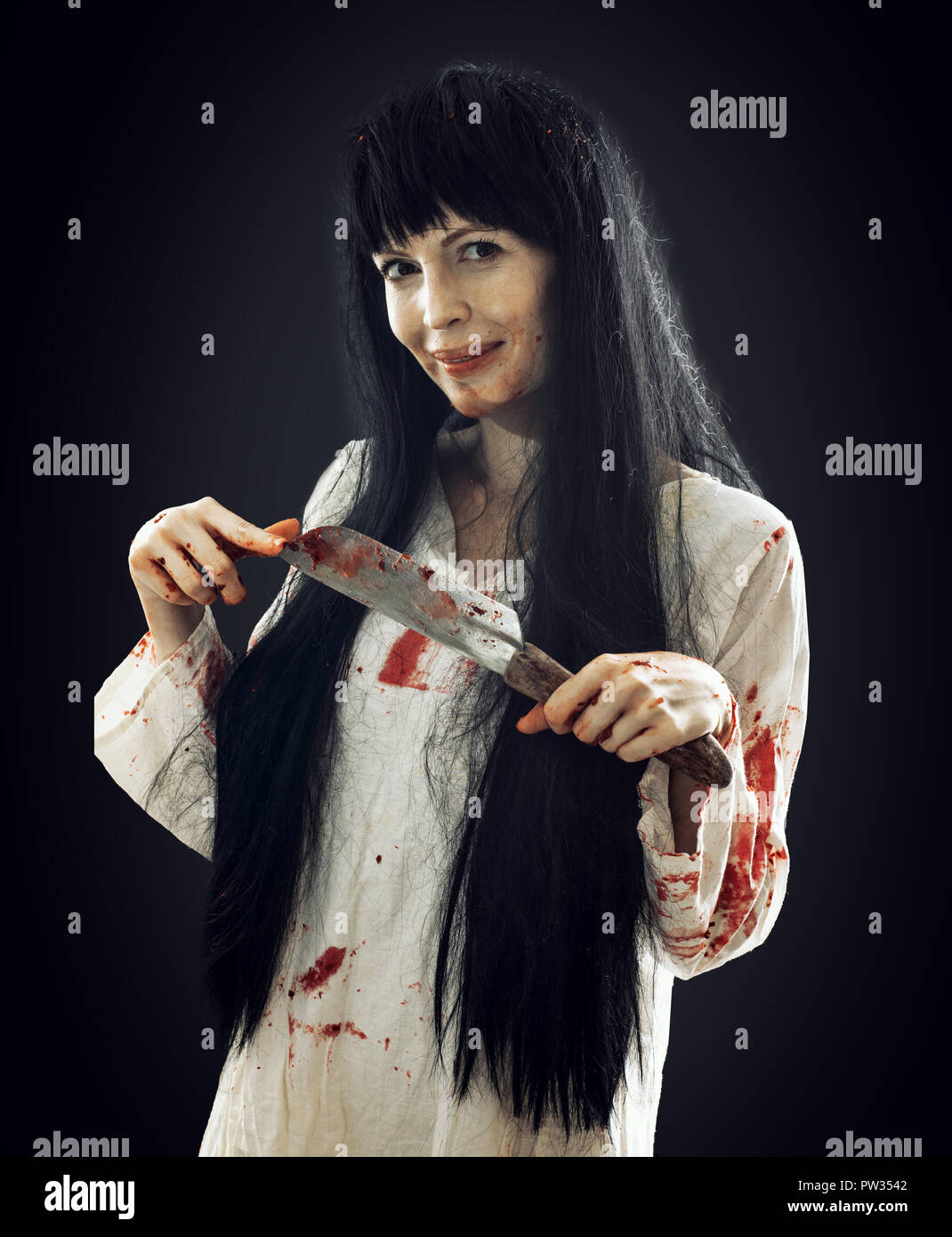 Halloween horror. Crazy bloody scary smiling maniac girl holding knife  butcher cleaver looks into camera on black background Stock Photo - Alamy