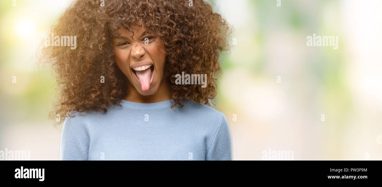 African american woman wearing a sweater sticking tongue out happy with ...