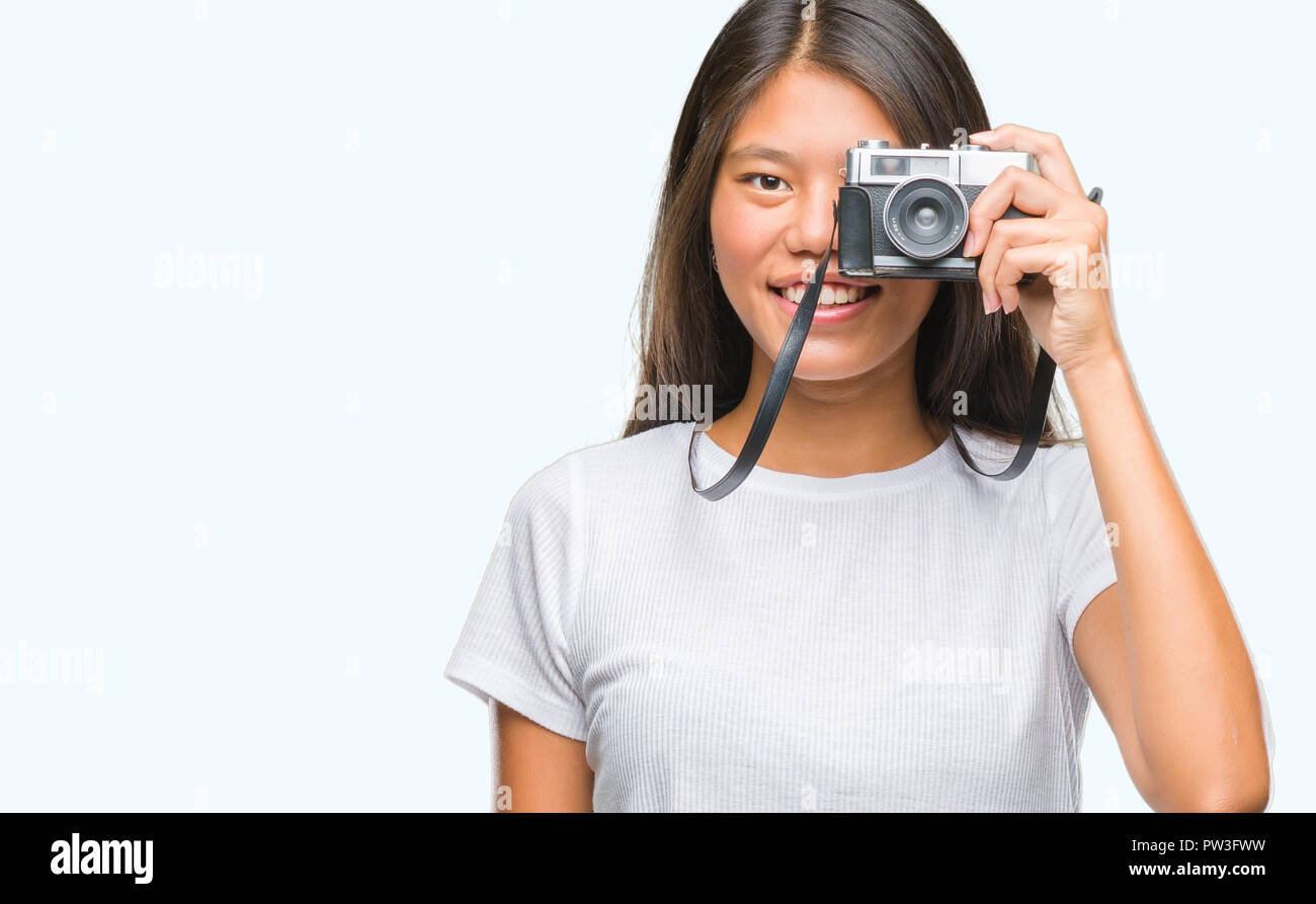Young asian woman holding vintagera photo camera over isolated background with a happy face standing and smiling with a confident smile showing teeth Stock Photo