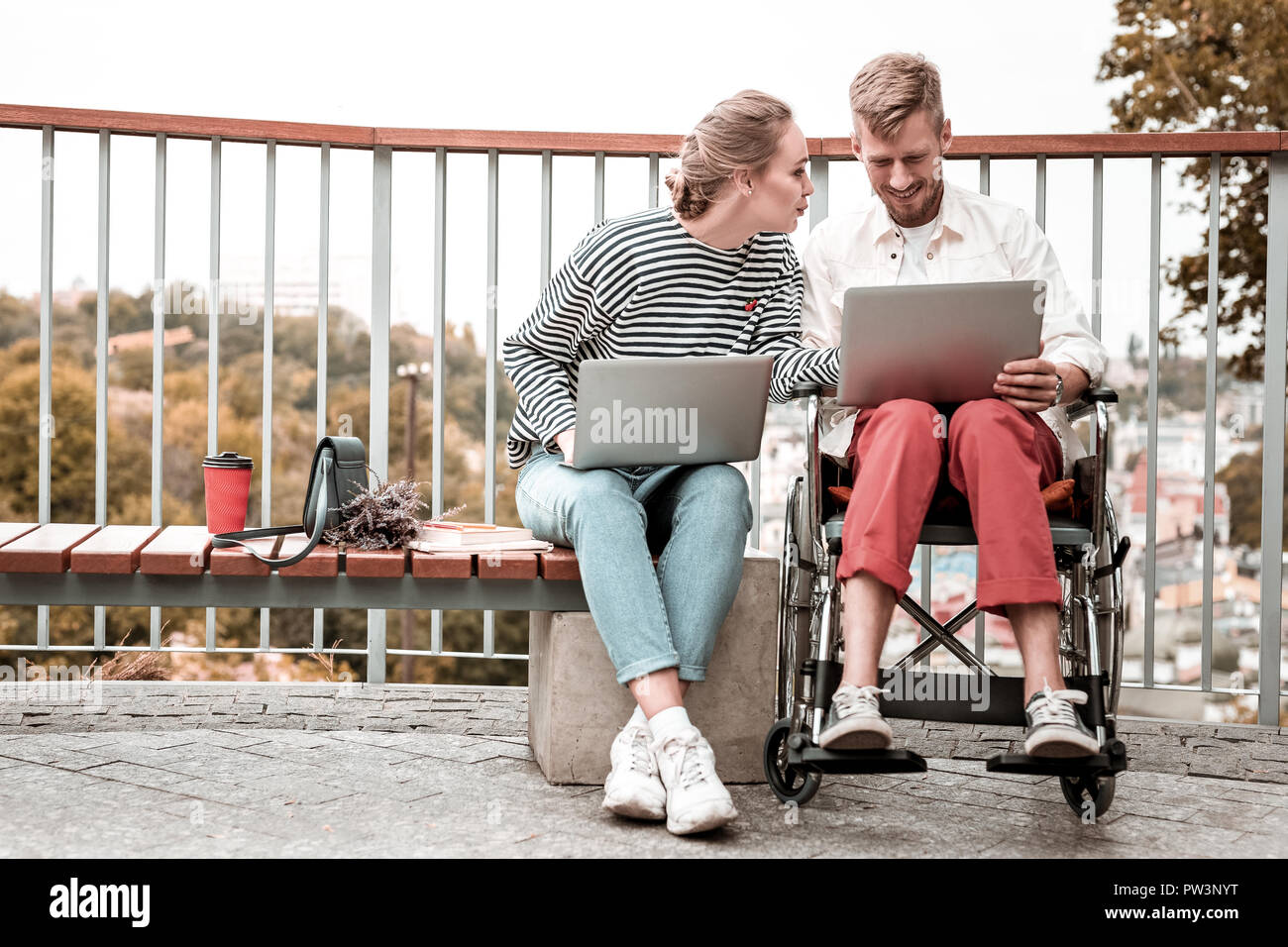 Disabled man sitting with colleague and working on laptop Stock Photo