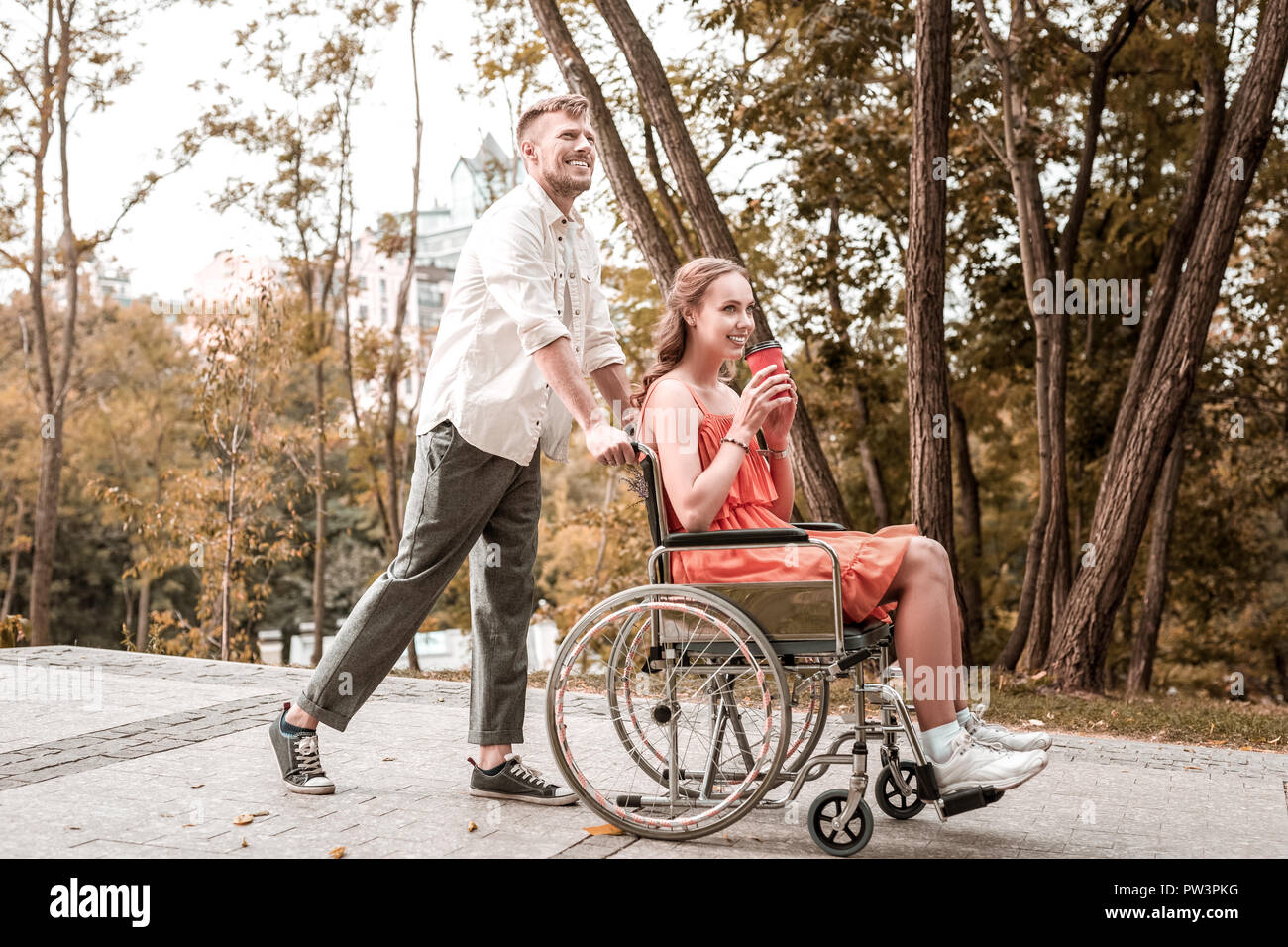 Happy man pushing the wheelchair of his girlfriend while walking in the park Stock Photo