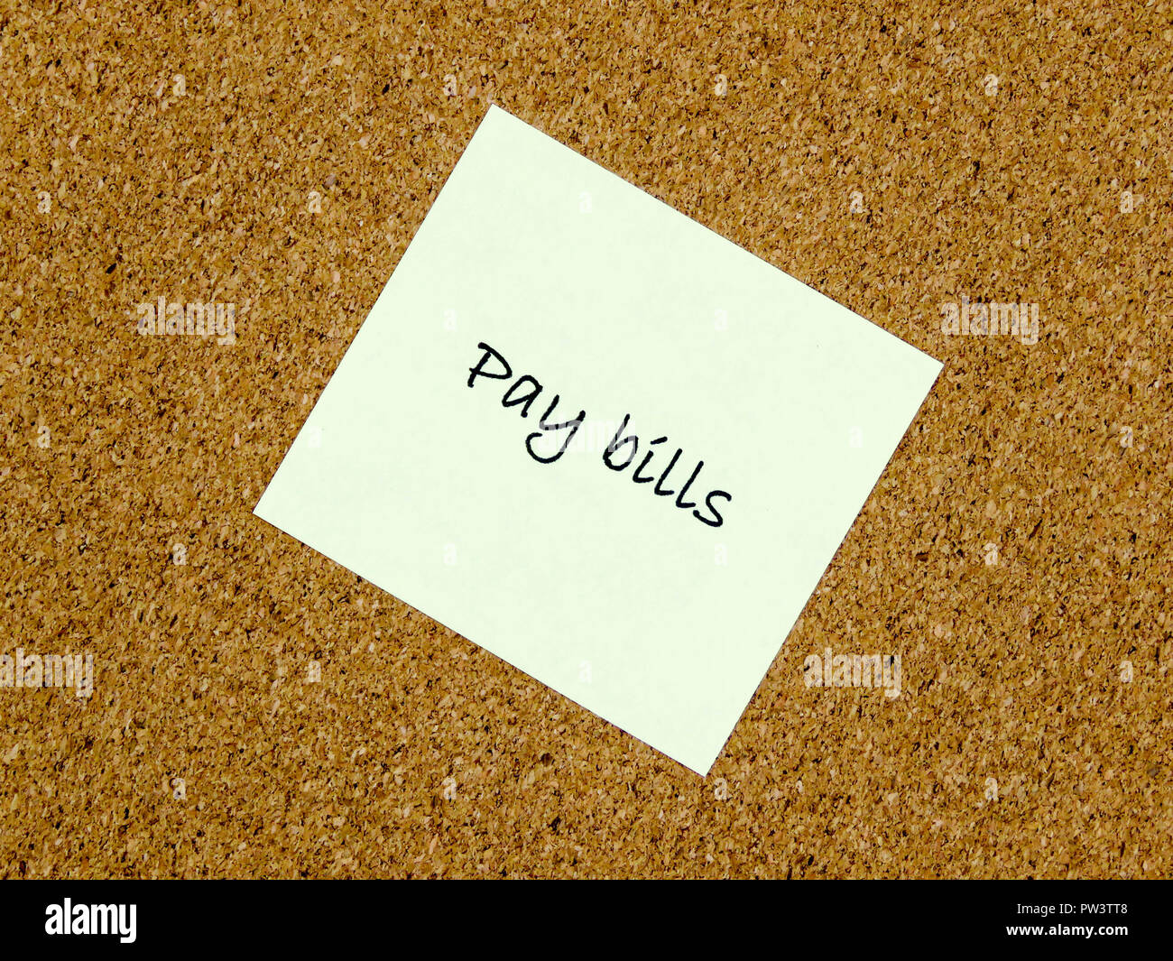 A yellow sticky note with pay bills written on it on a cork board background Stock Photo