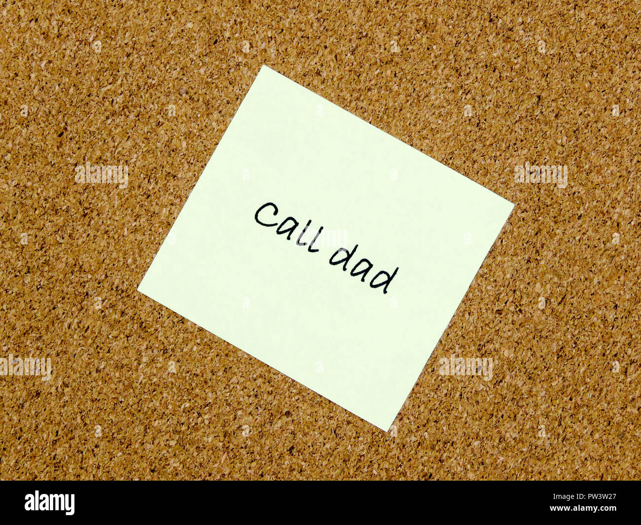 A yellow sticky note with call dad written on it on a cork board ...