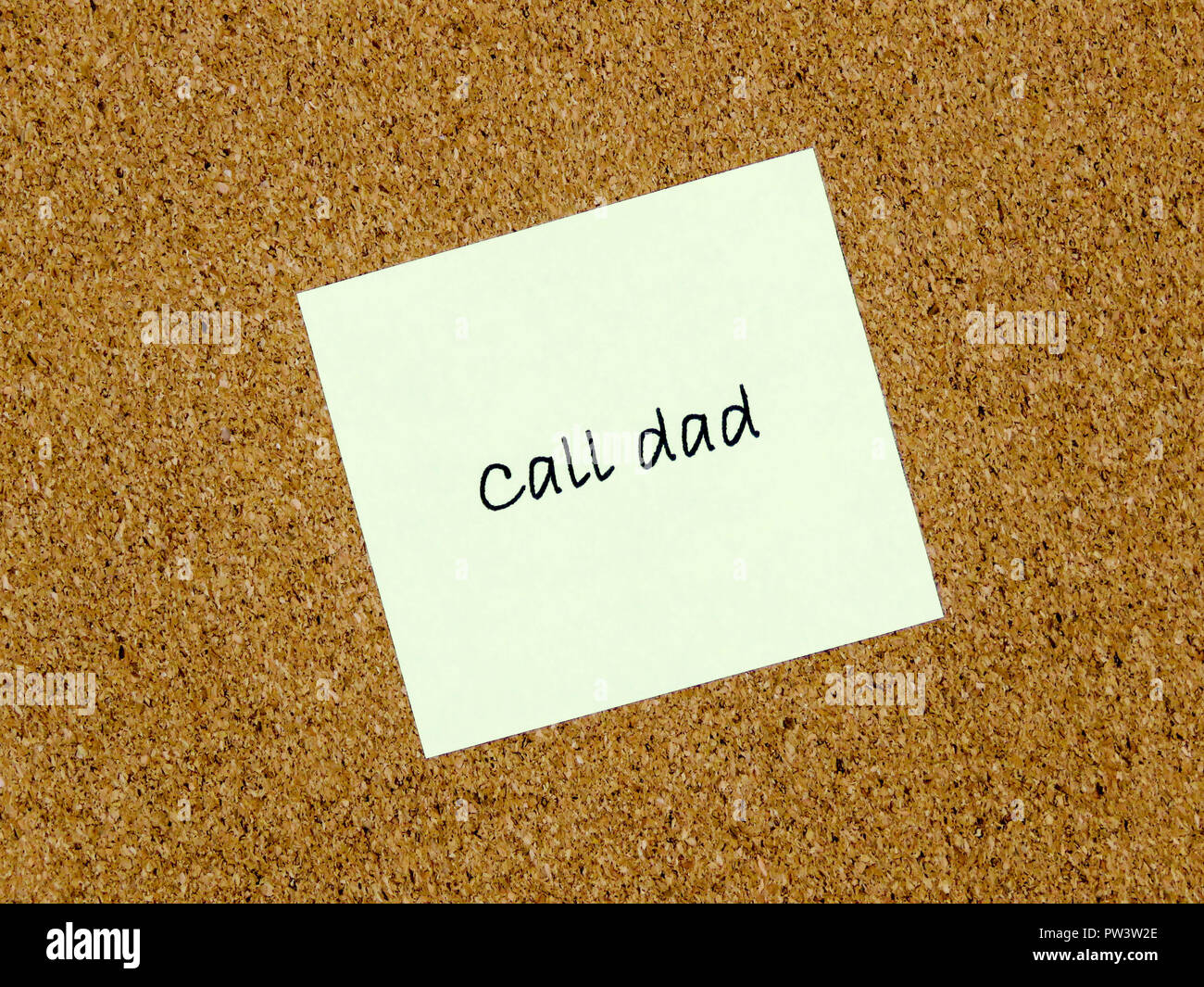 A yellow sticky note with call dad written on it on a cork board ...