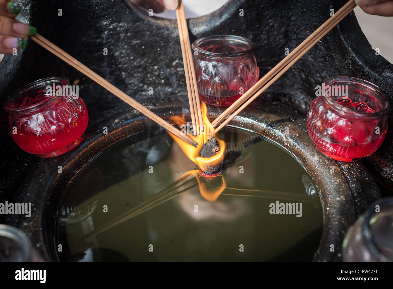 Three hand holding incense sticks over a burning candle in oil in a