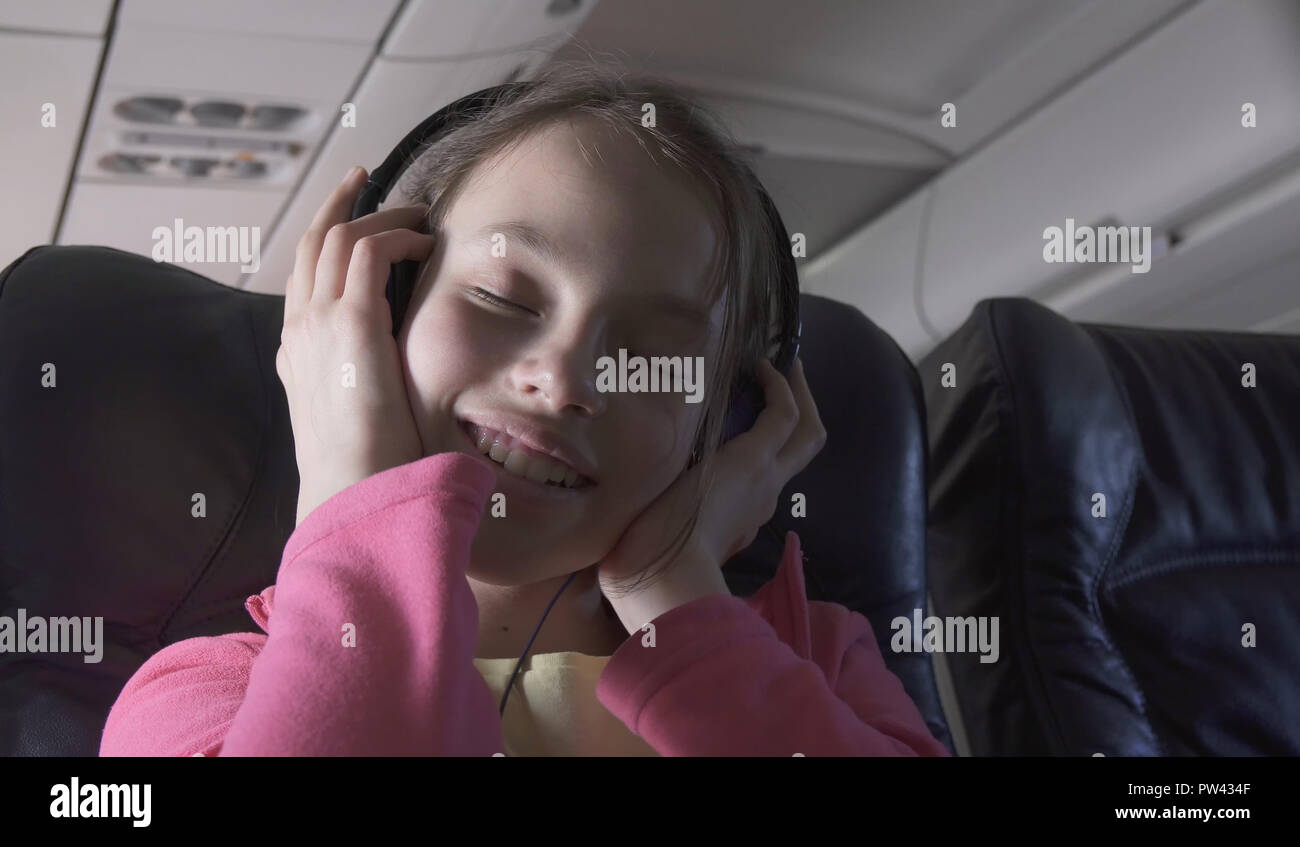 Cheerful teenage girl listens to music on headphones in the cabin of plane while traveling Stock Photo