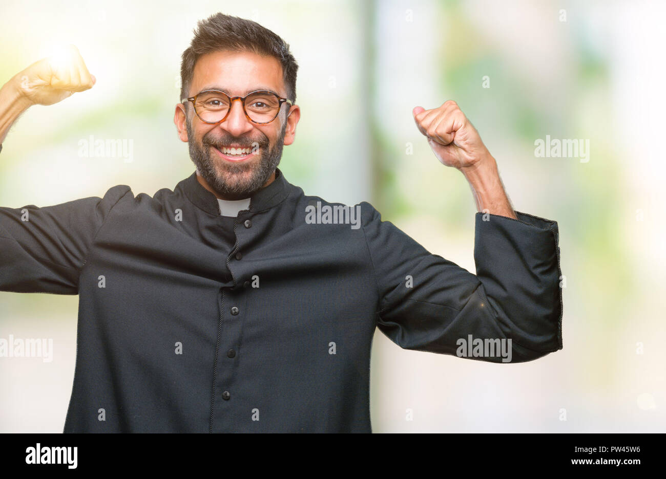 Adult hispanic catholic priest man over isolated background showing arms muscles smiling proud. Fitness concept. Stock Photo