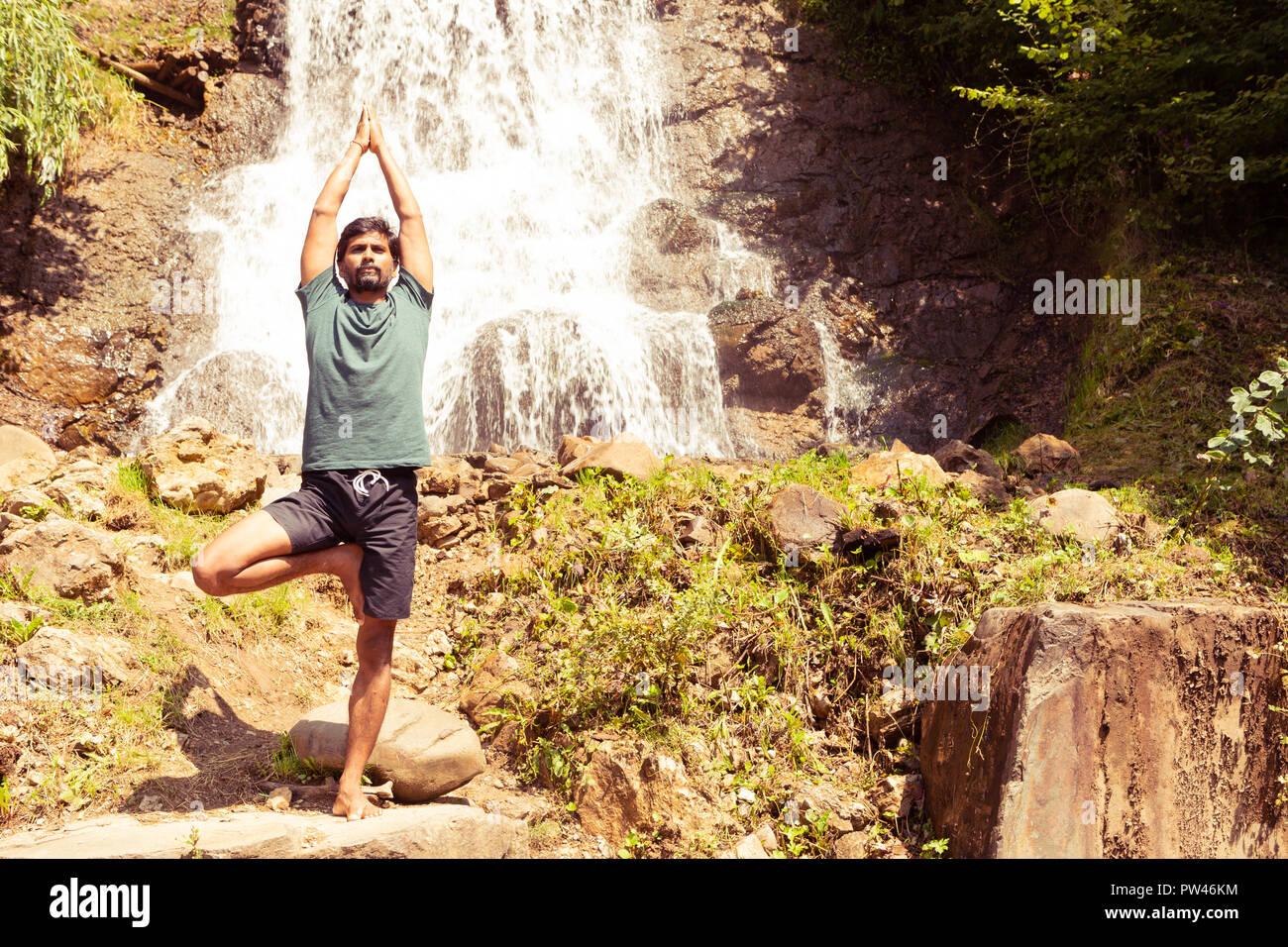 Tree yoga position practiced near waterfall by indian yogi with natural background Stock Photo