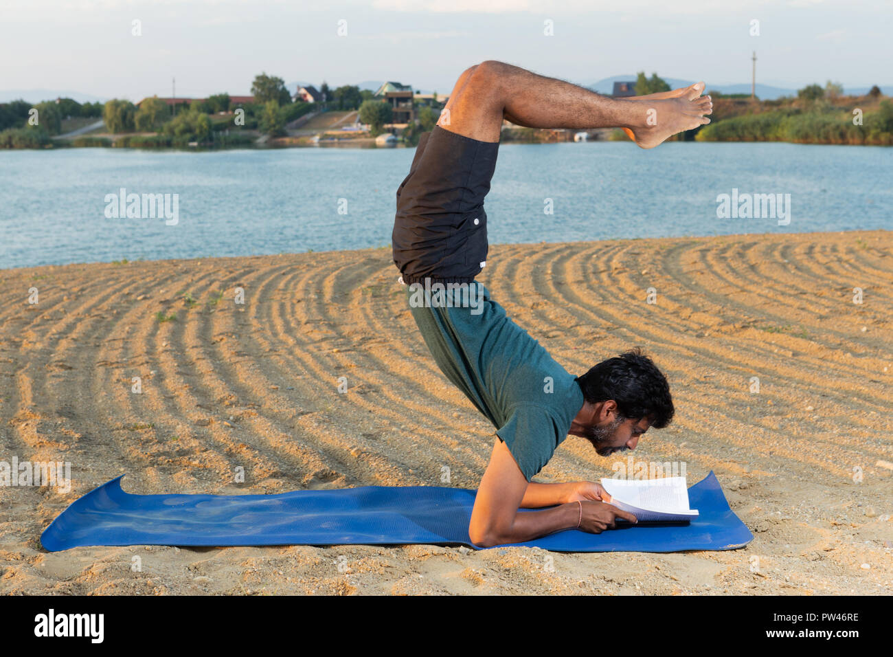 Indian yoga master reading a book in headstand position with natural