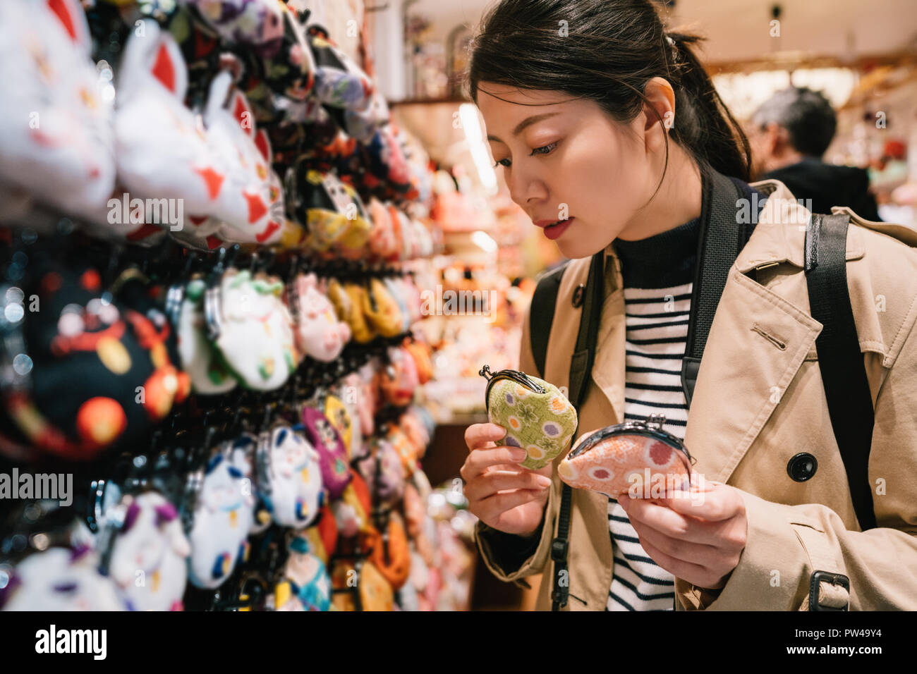 lovely female tourist standing in the souvenir store and choosing coin bags for her friends. traveler buying gifts concept. beautiful girl holding two Stock Photo
