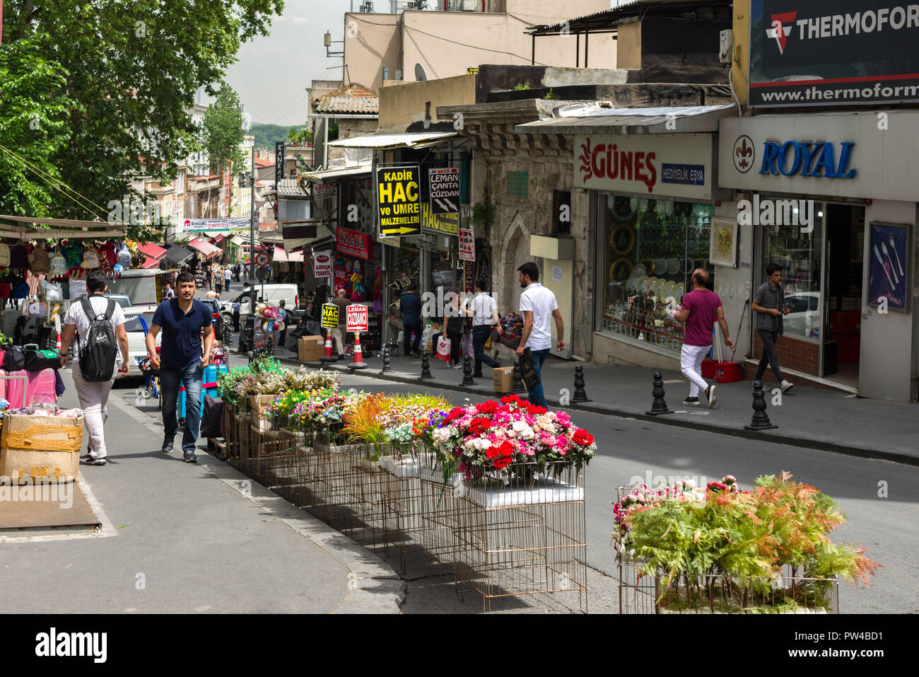 A hilly street scene with people walking past shops, plastic flowers are on display in the foreground, Istanbul, Turkey Stock Photo