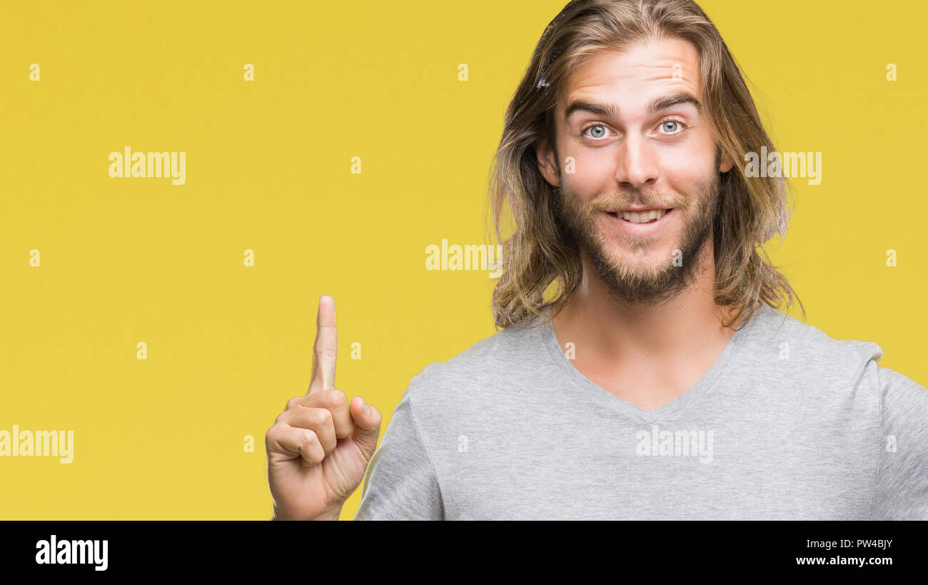 Young handsome man with long hair over isolated background holding ...