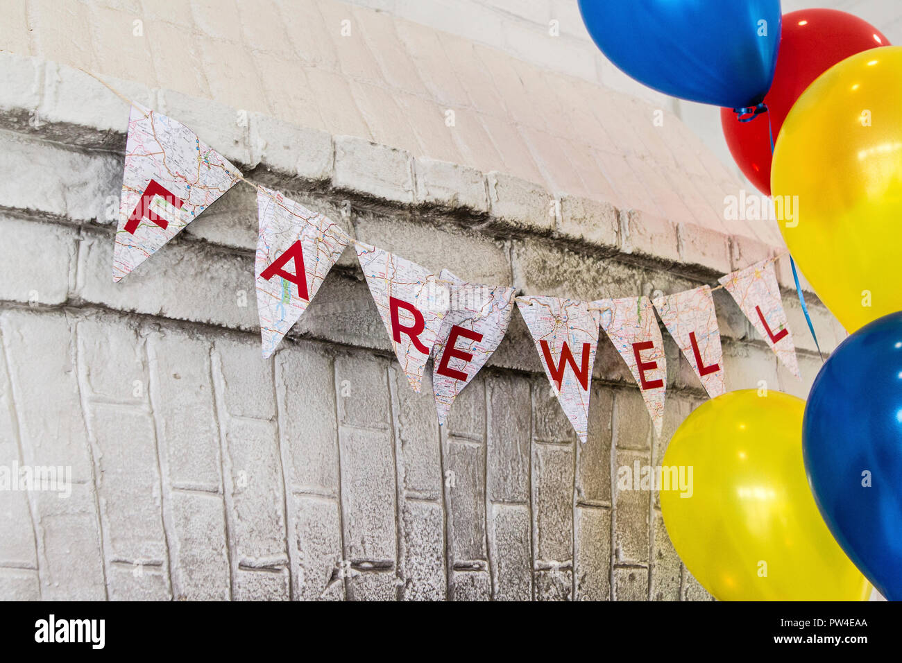 Farewell text on buntings by colorful helium balloons hanging against wall Stock Photo