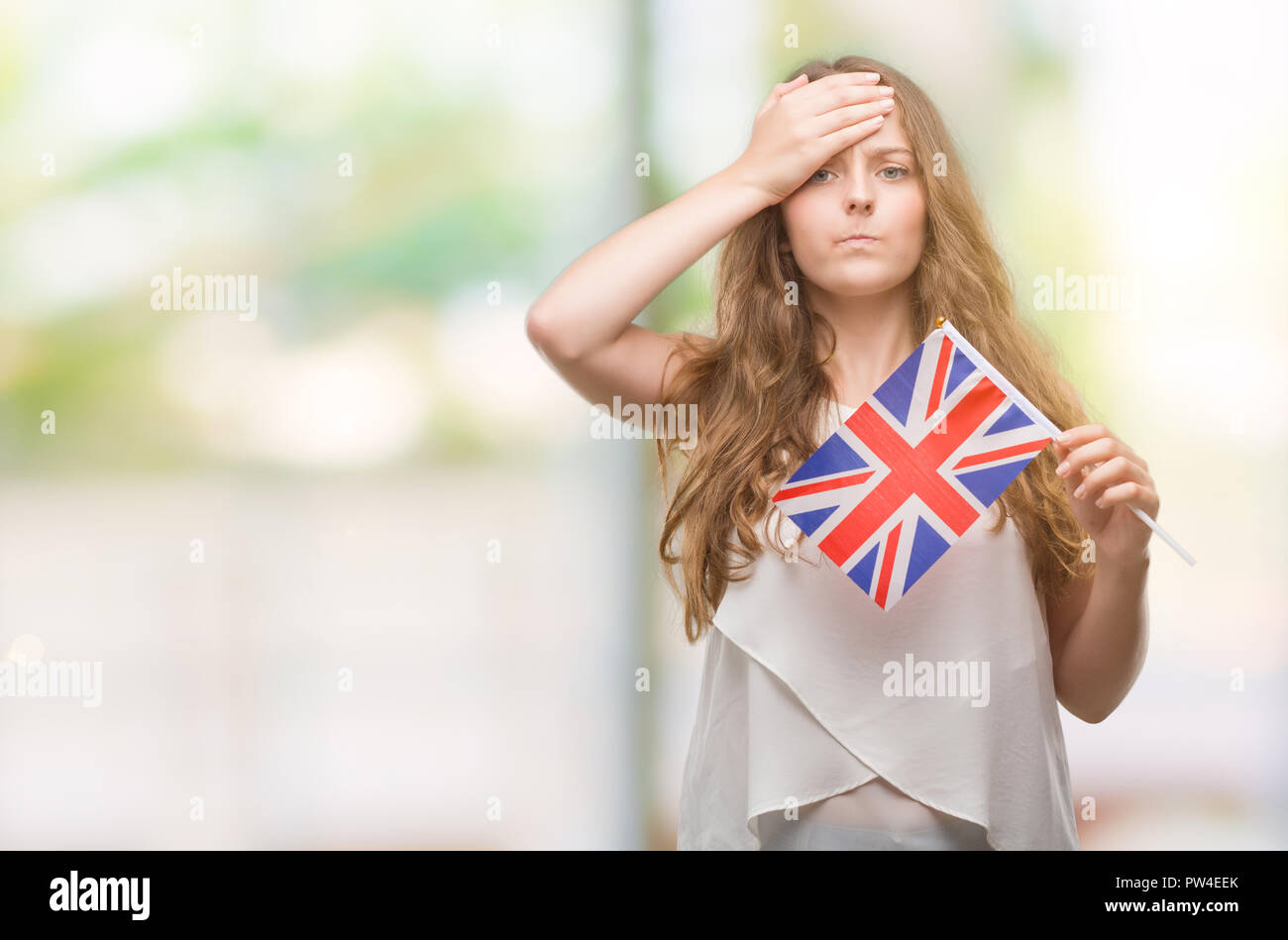 Young blonde woman holding flag of UK stressed with hand on head, shocked with shame and surprise face, angry and frustrated. Fear and upset for mista Stock Photo