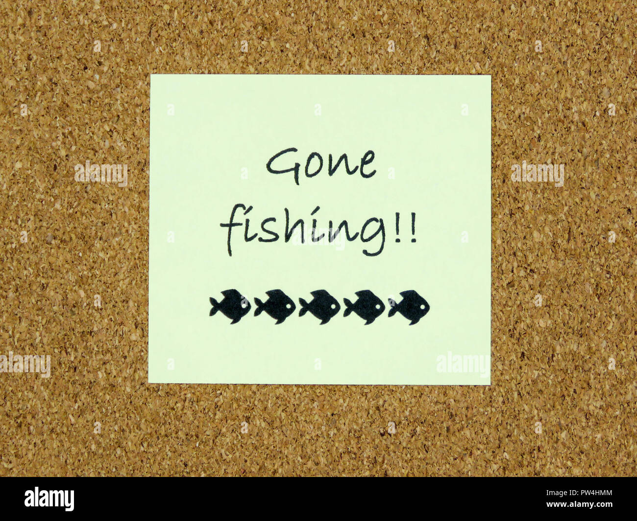 A yellow sticky note with gone fishing written on it on a cork board
