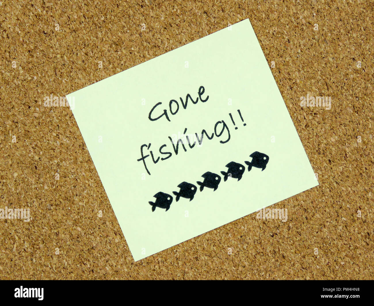 A yellow sticky note with gone fishing written on it on a cork board