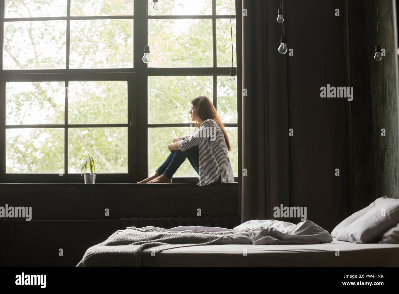 Lonely sad young woman sitting on windowsill at home Stock Photo - Alamy