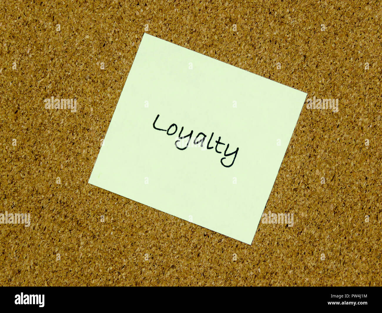 A yellow sticky note with loyalty written on it on a cork board ...