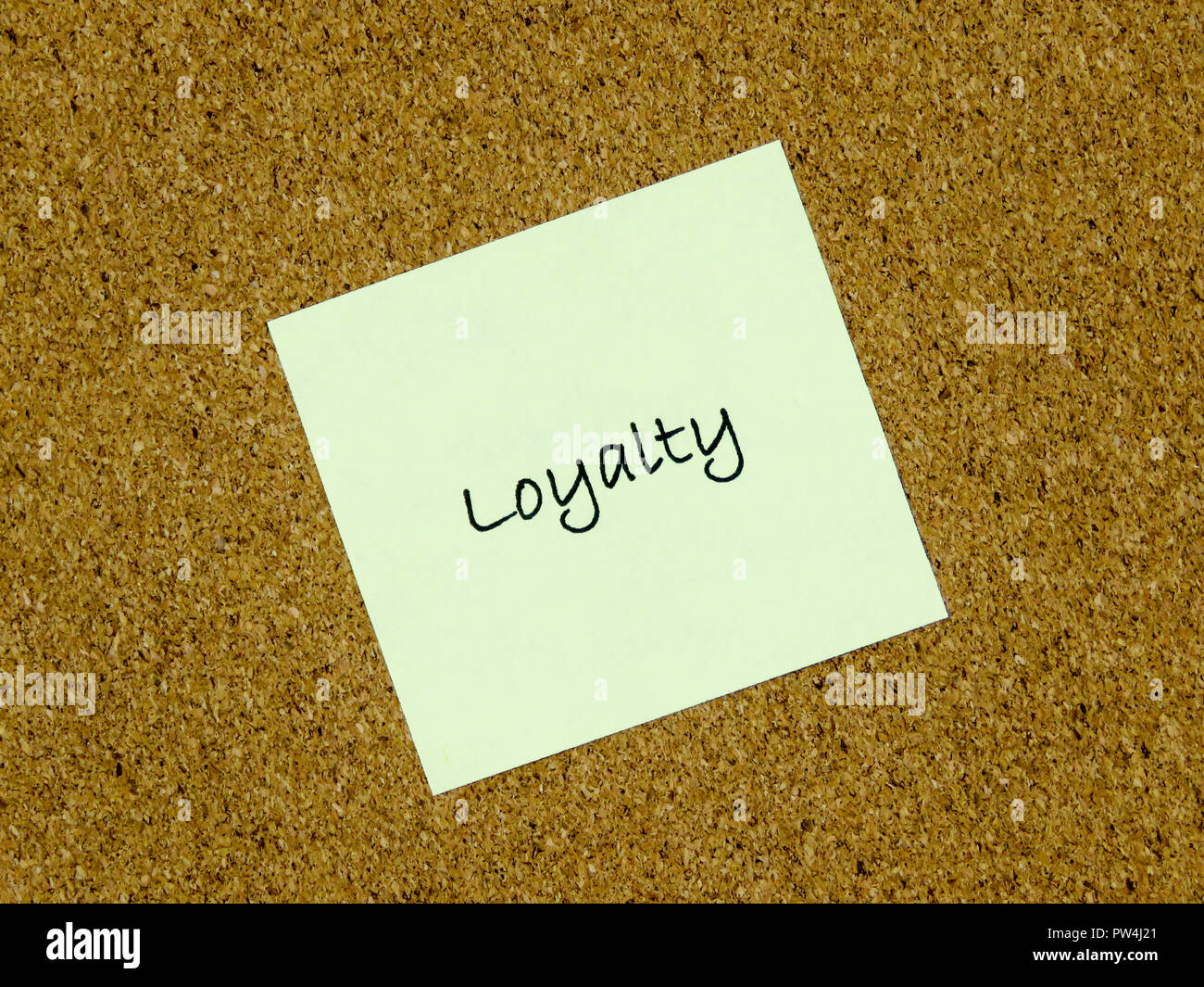 A yellow sticky note with loyalty written on it on a cork board ...