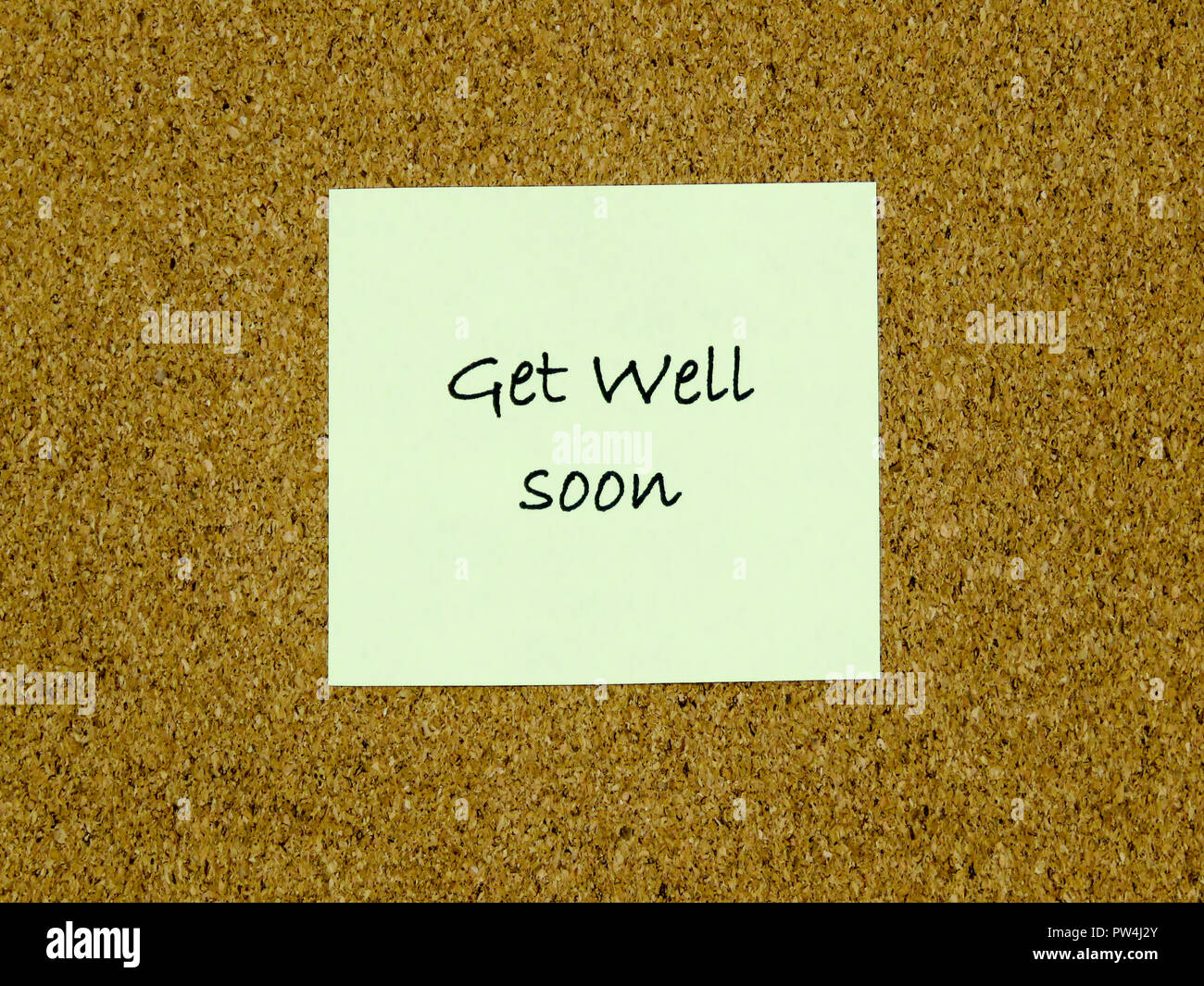 A yellow sticky note with get well soon written on it on a cork board background Stock Photo