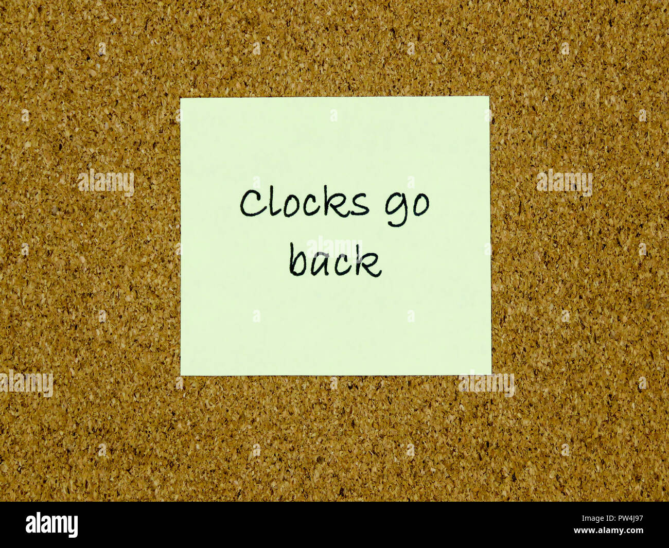 A yellow sticky note with clocks go back written on it on a cork board background Stock Photo