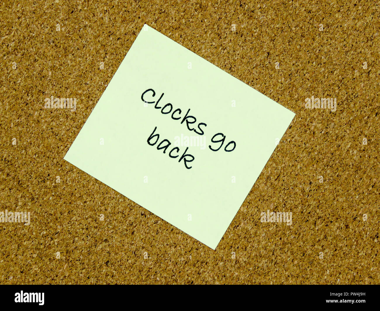 A yellow sticky note with clocks go back written on it on a cork board background Stock Photo