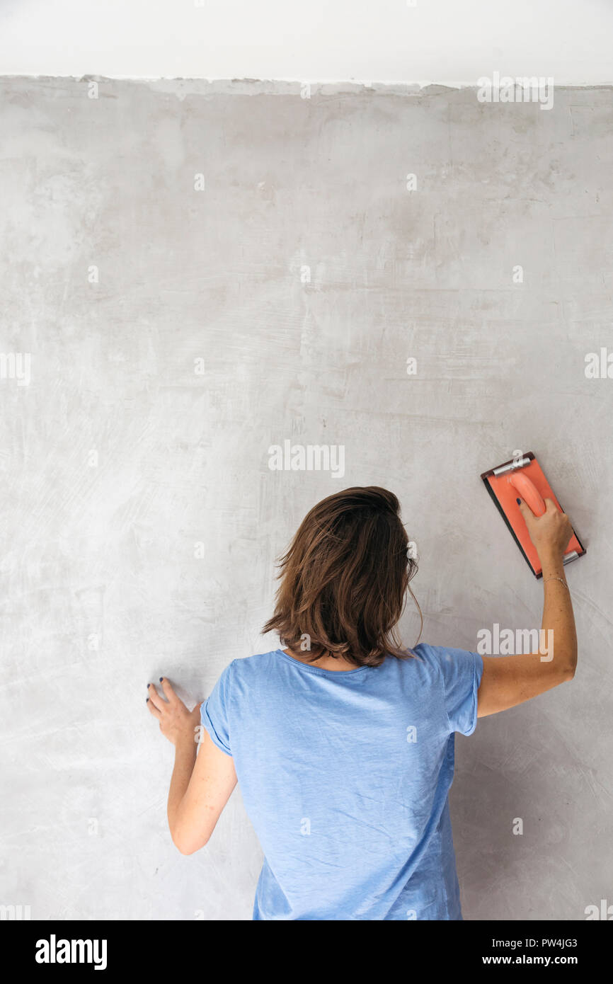 Woman sanding wall with hand sander during renovation Stock Photo
