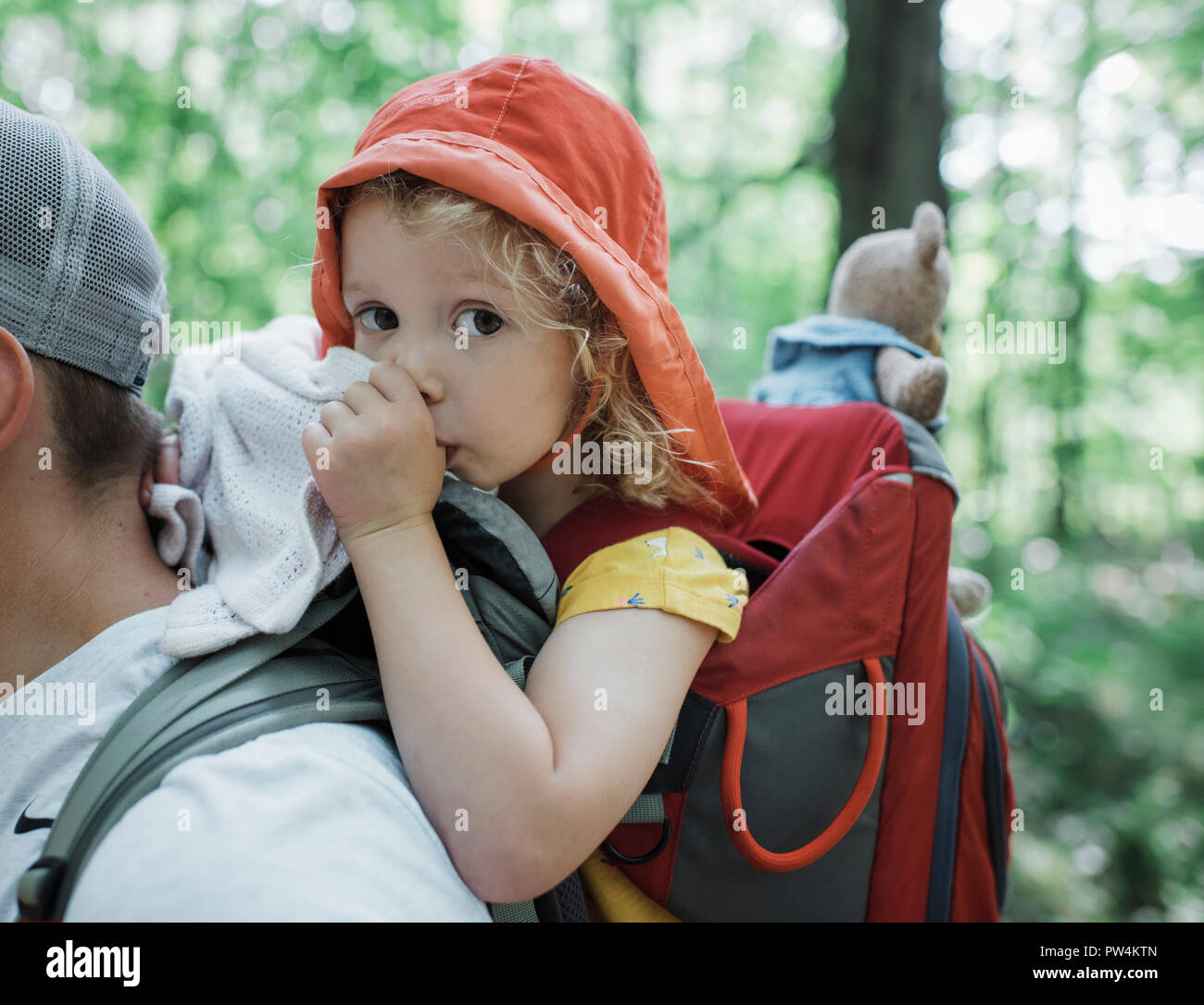 Portrait of cute daughter thumb sucking while being carried by father in forest Stock Photo