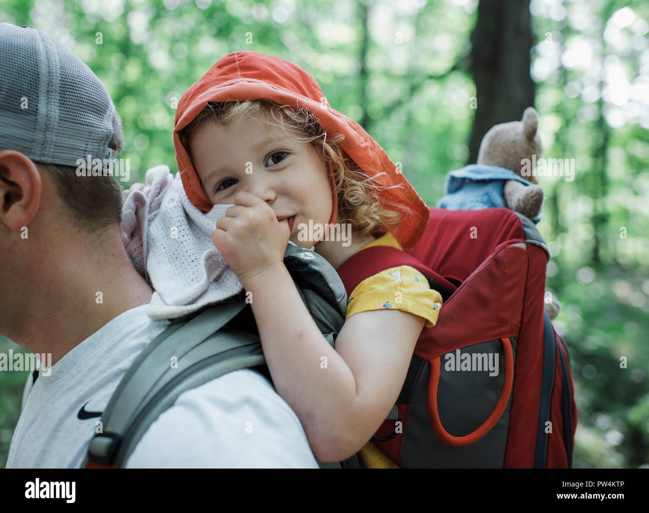Portrait of cute happy daughter thumb sucking while being carried by father in forest Stock Photo