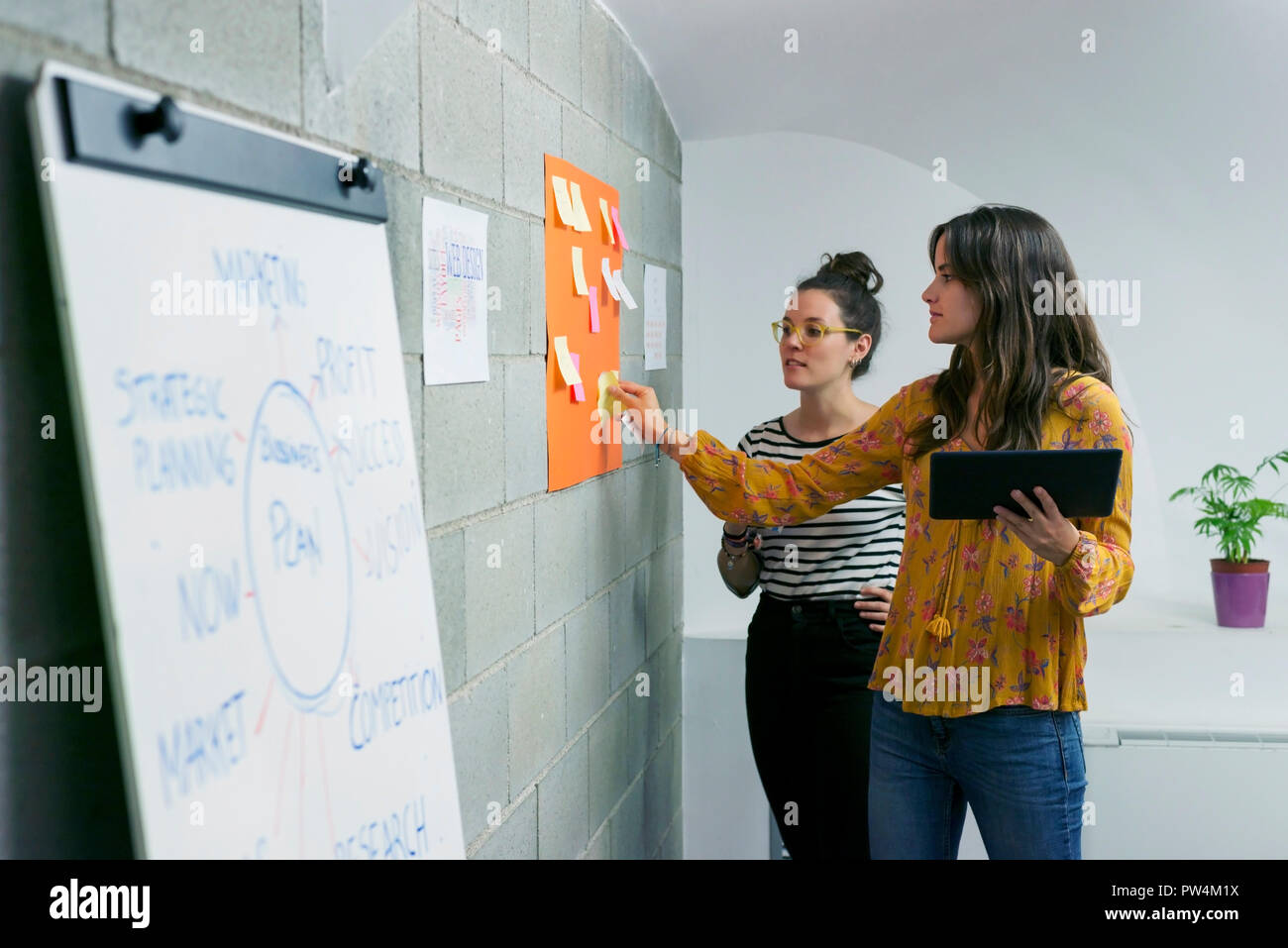Female colleagues discussing over adhesive notes while standing in creative office Stock Photo