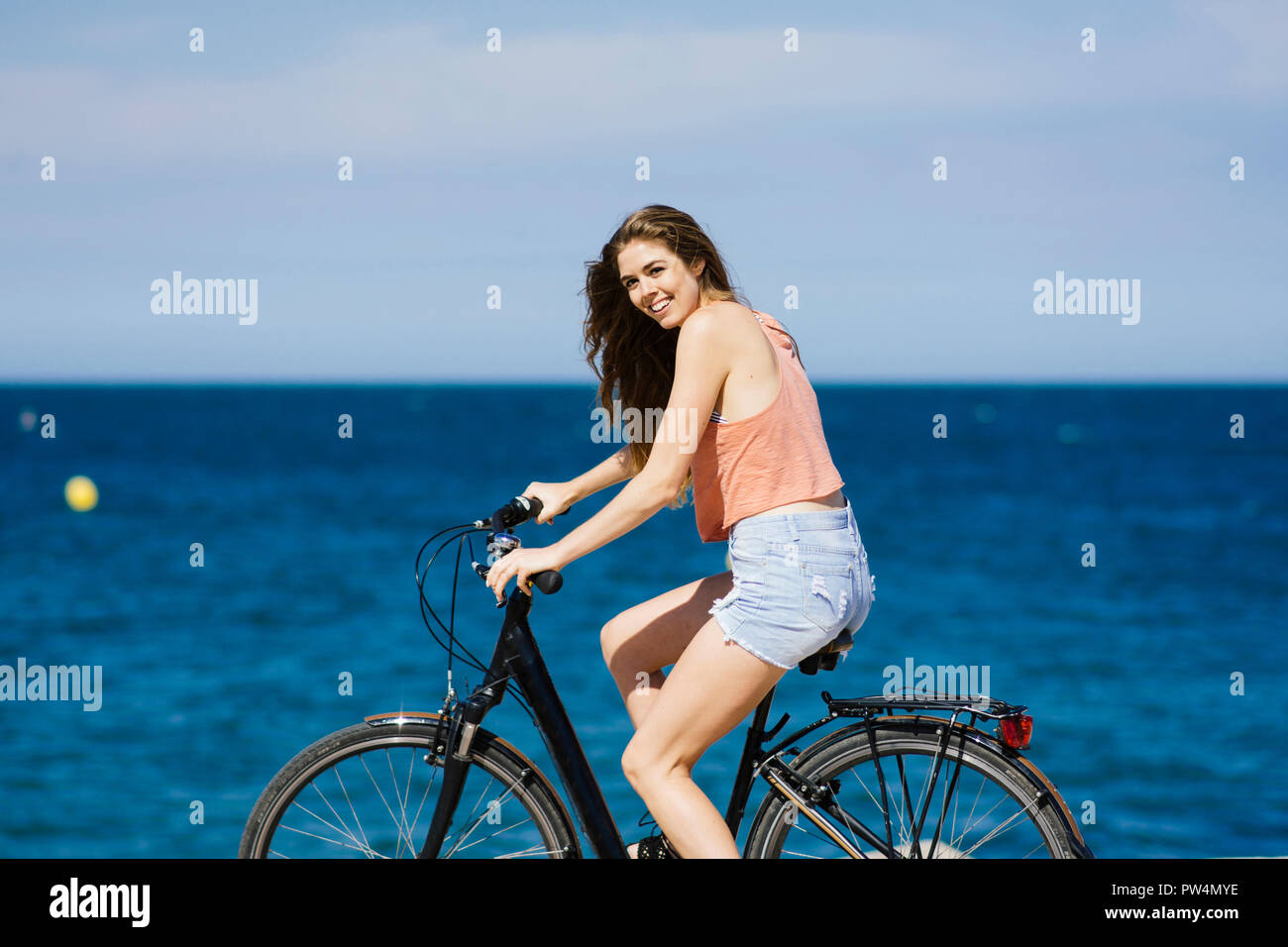 Happy woman riding bicycle at beach against sky during sunny day Stock Photo