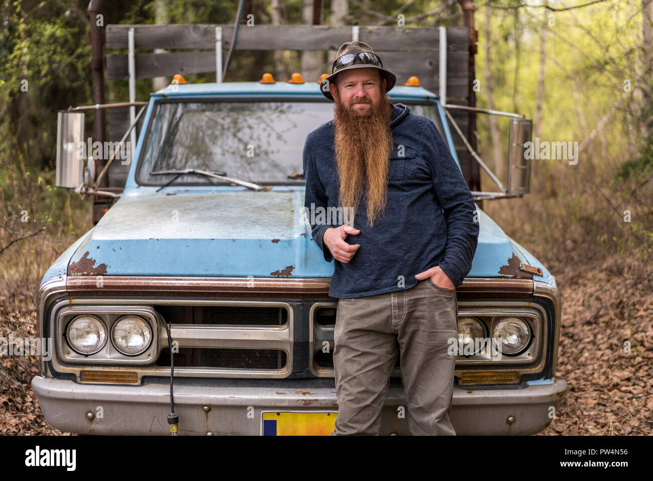 Portrait of confident bearded man standing against old pick-up truck in forest Stock Photo