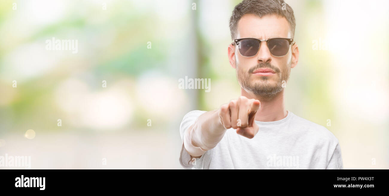 Young tattooed adult man wearing sunglasses pointing with finger to the ...