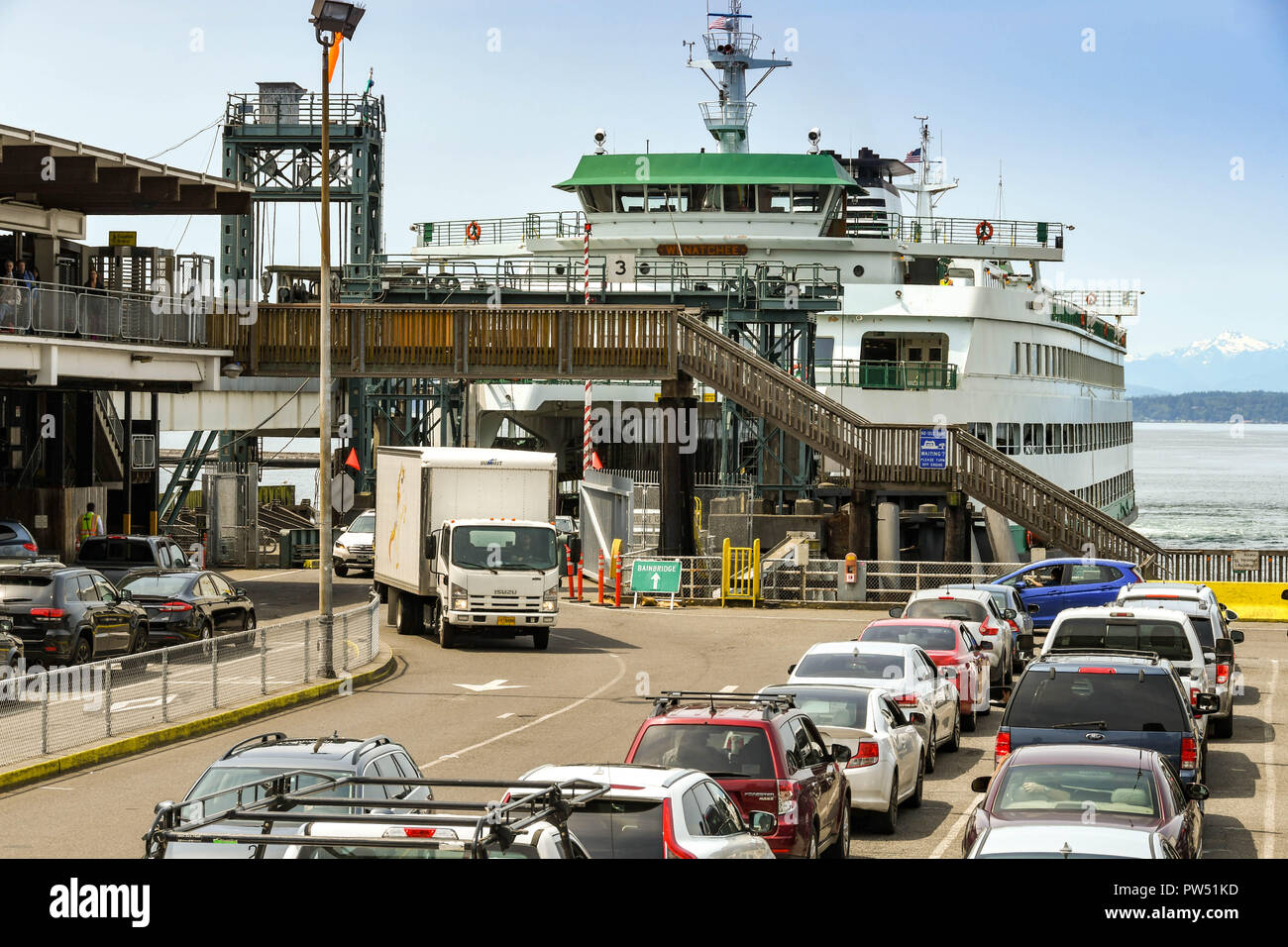 SEATTLE, WASHINGTON STATE, USA - JUNE 2018: Rows of cars waiting on the harborside in Seattle to drive on to a large ferry while other vehicles drive  Stock Photo