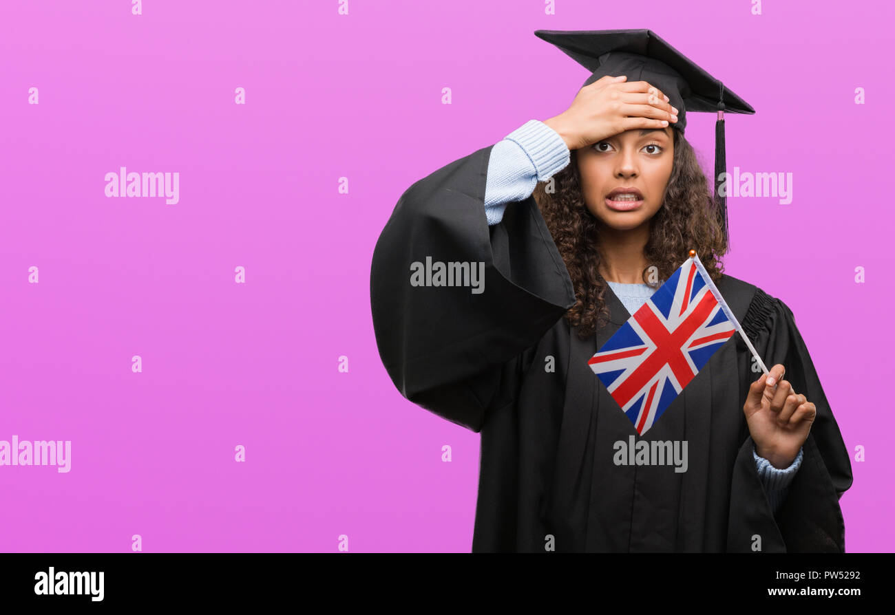 Young hispanic woman wearing graduation uniform holding flag of UK stressed with hand on head, shocked with shame and surprise face, angry and frustra Stock Photo