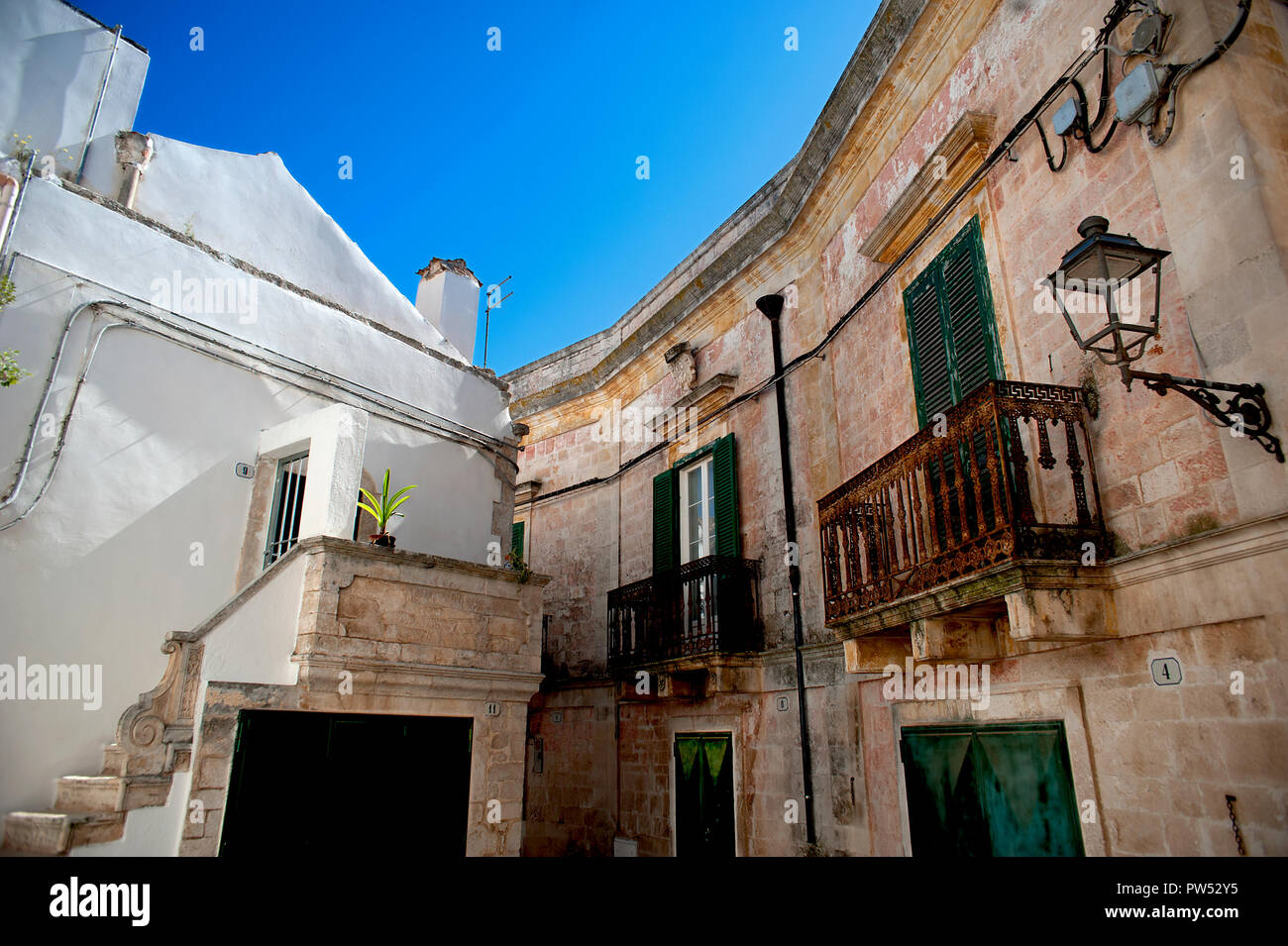 Stone and whitewashed houses with rusty balconies and green wooden shutters in the old quarter of Ceglie in Puglia, southern Italy. Stock Photo