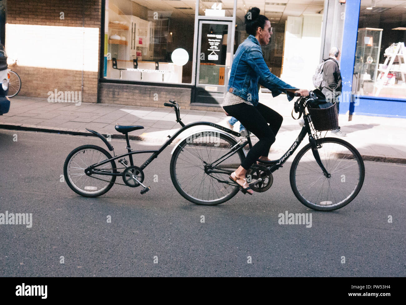 Lady on her bicycle with a basket and a Coupler Attachment also known as a Trail Gator Child also known as a Kid Bike Tow Stock Photo Alamy