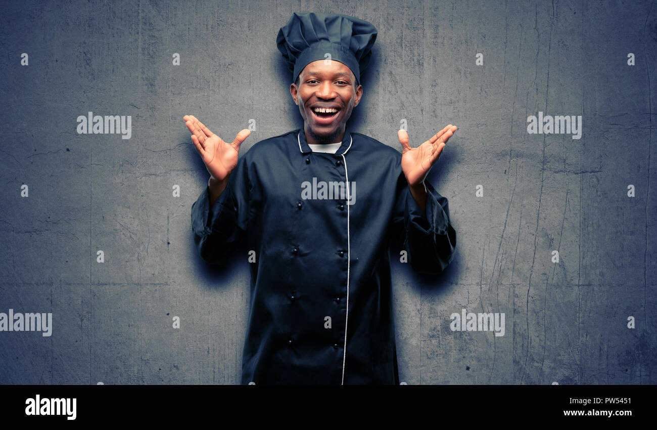 Young black cook wearing chef hat happy and surprised cheering