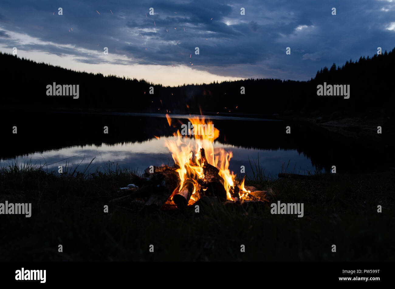 Campfire after sunset in the mountains next to a lake Stock Photo