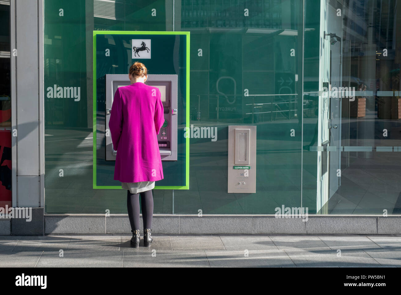 Woman wearing a pink coat at a Lloyds Bank cash machine. London, UK Stock Photo