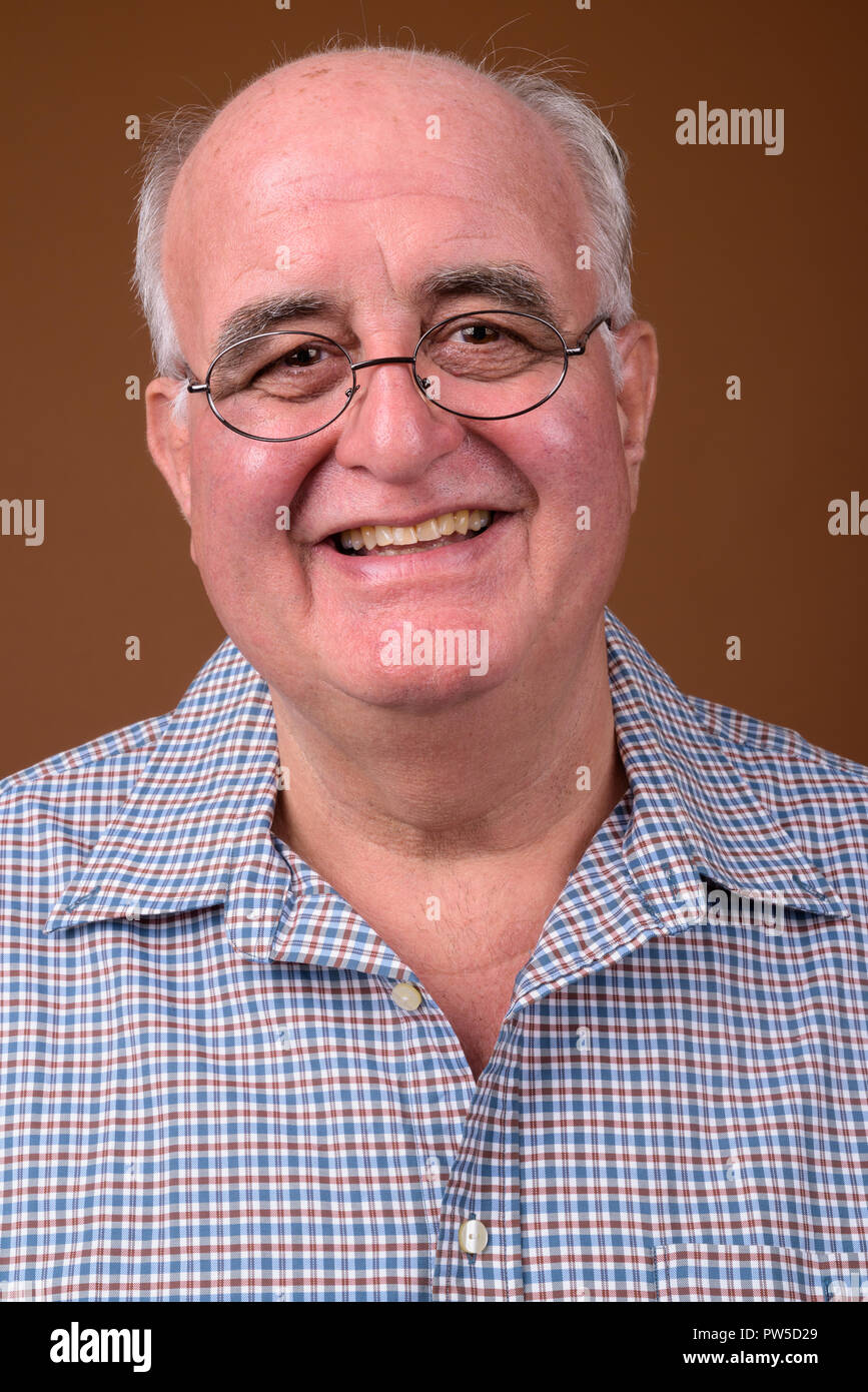 Overweight senior man wearing eyeglasses against brown backgroun Stock