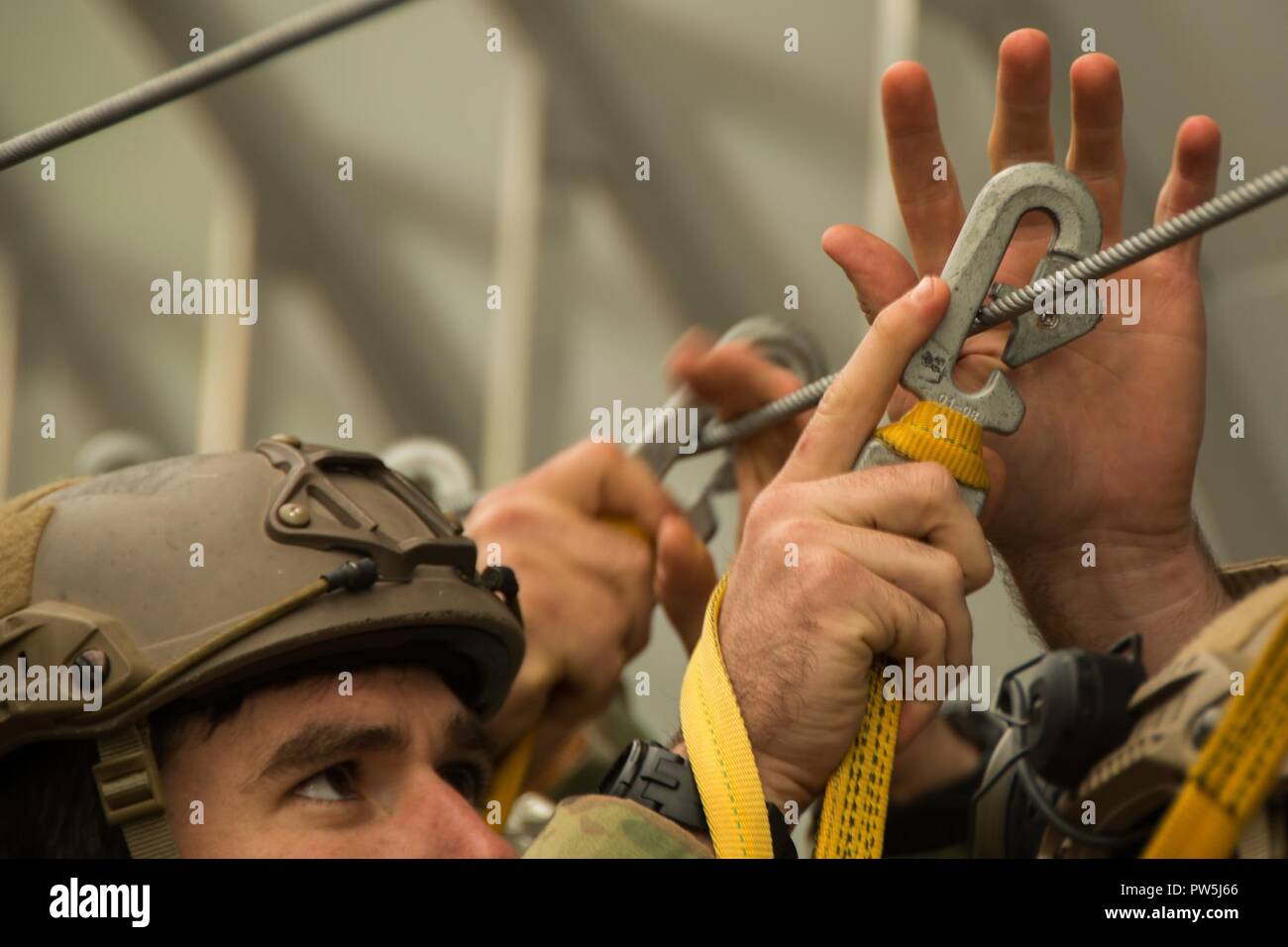A Green Beret assigned to 1st Battalion, 10th Special Forces Group  (Airborne), attaches the snap hook of his universal static line to the  anchor-line cable of a C-130 Hercules mock-up during pre-jump
